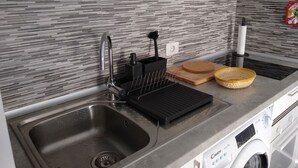 A modern kitchen with a stainless steel sink, a black drying rack, a wooden cutting board, and a white washing machine. - cosy appartment in a residencial development near the sea (Puerto del Carmen)