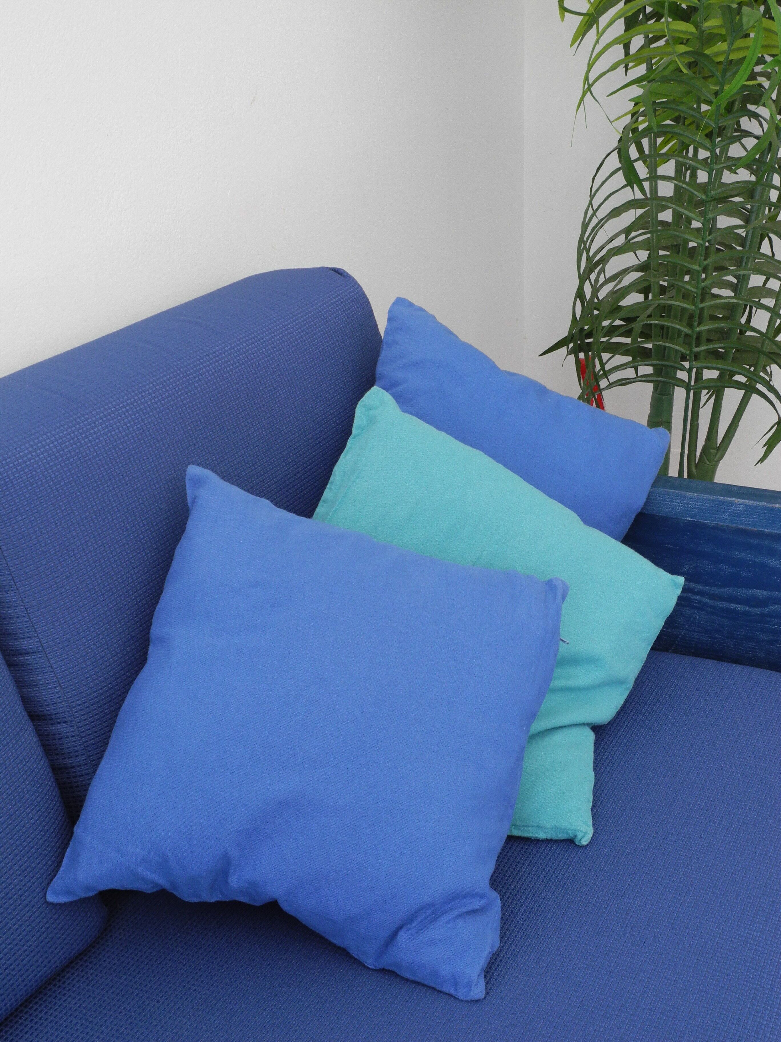 Un canapé bleu avec deux coussins, l’un bleu clair et l’autre bleu foncé, adossé à un mur blanc.