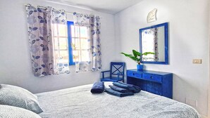 A bedroom with a bed, a chair, a dresser, a mirror, and a window with curtains. - cosy appartment in a residencial development near the sea (Puerto del Carmen)