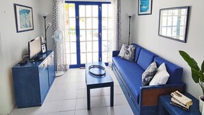 A living room with a blue sofa, a small table, a desk with a computer, and a window with curtains. - cosy appartment in a residencial development near the sea (Puerto del Carmen)