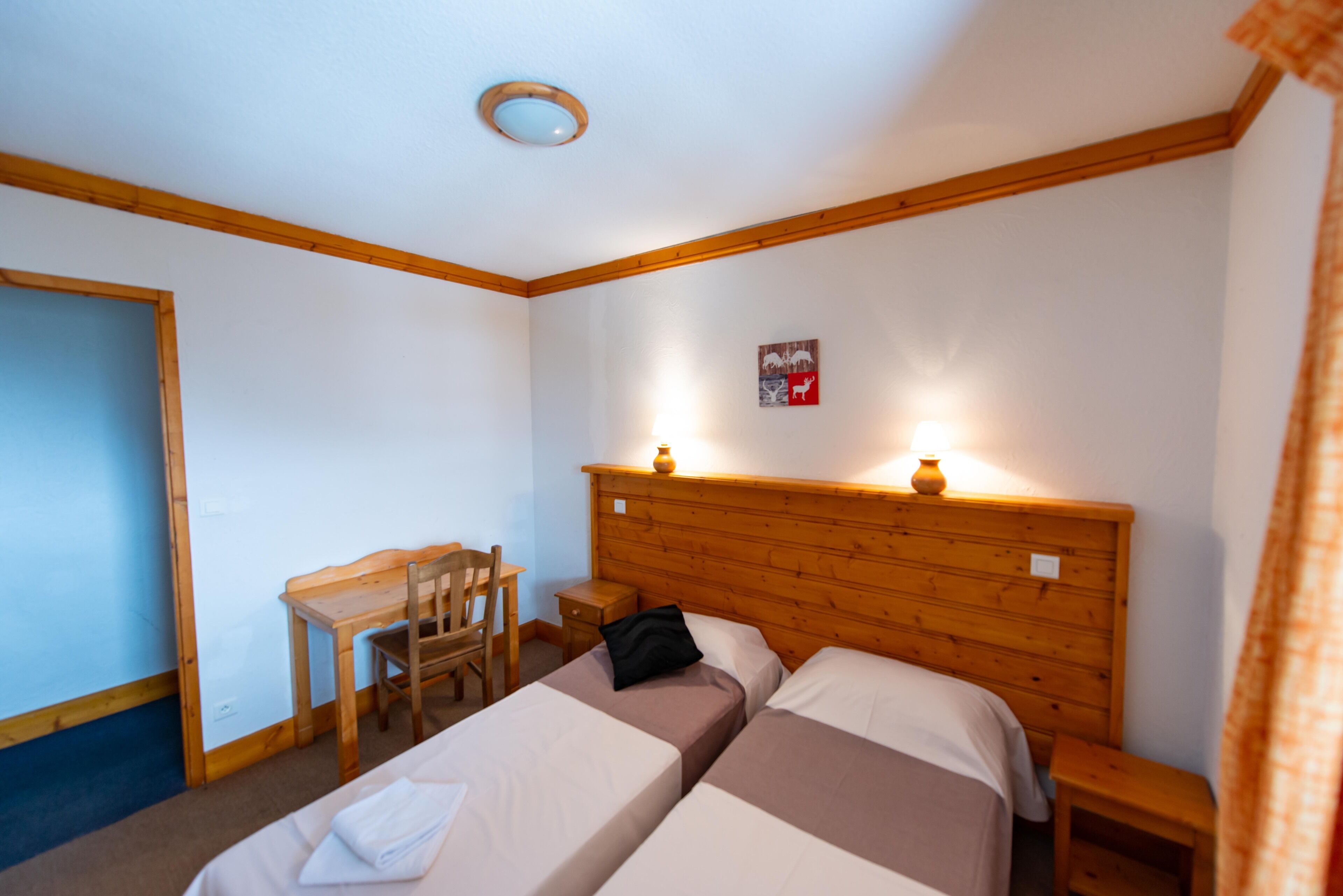 A room with two beds, a wooden desk, a chair, and a small table.