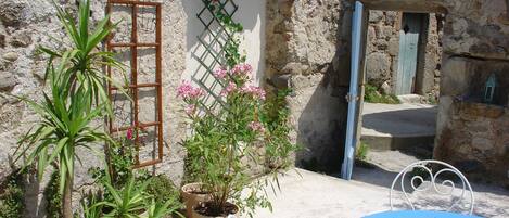 Une cour intérieure avec un mur en pierre, des plantes en pot, une table en métal bleue et une chaise en métal.