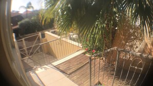Vista panorámica de una escalera que lleva a un balcón con una palmera y flores rojas.
