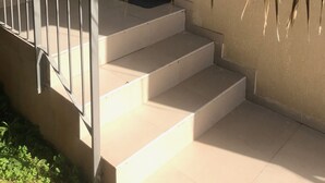 Una escalera con barandilla metálica que lleva a una plataforma, rodeada de follaje.