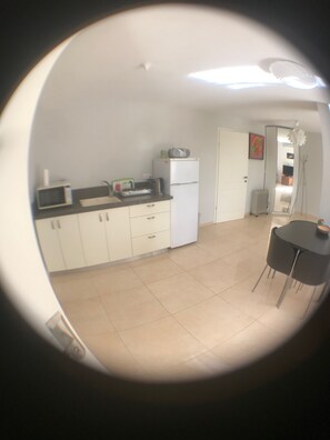 Compact kitchen with microwave, toaster, and refrigerator, adjacent to a dining area with a table and chairs.