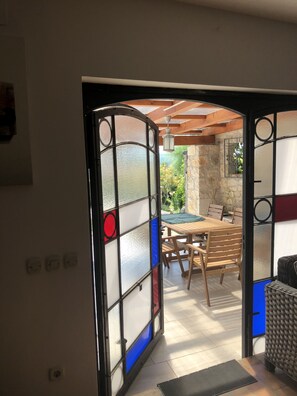 Una puerta abierta que da a un patio al aire libre con una mesa y sillas de madera.