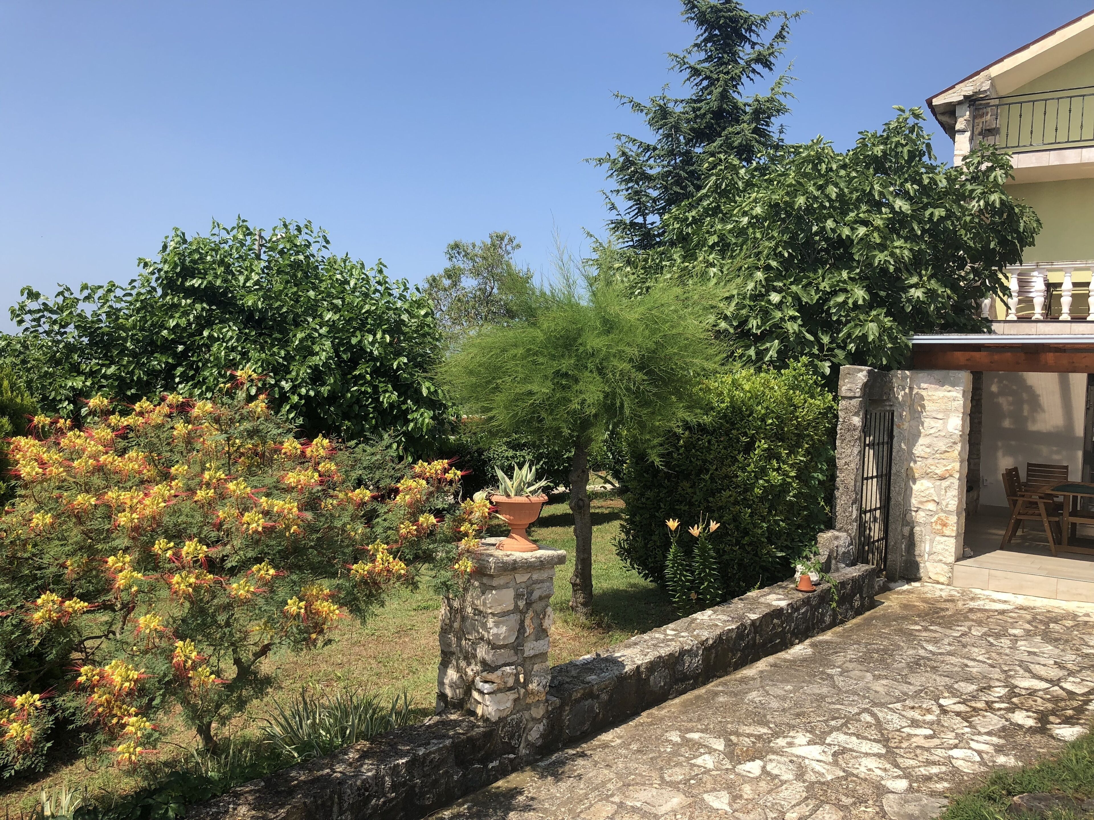 Un chemin de pierres mène à un patio abrité, bordé d’un mur en pierre et agrémenté d’une table en bois.