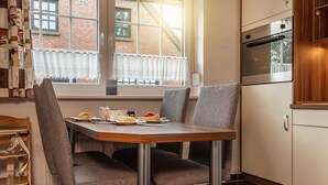 Cocina compacta con una mesa de comedor, sillas y una ventana con vista a un edificio de ladrillo.