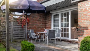 Un patio con una mesa, sillas, una sombrilla y un muro de ladrillo.