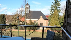 A balcony with wicker furniture, a brick building with a tower in the background, and a clear sky. - Suite with terrace and view of the church, lake access - Ferienhof Löschebrand (Bad Saarow)