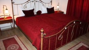 A neatly made bed with a red bedspread and matching pillows, a metal headboard, and two bedside tables with lamps. - Suite with terrace and view of the church, lake access - Ferienhof Löschebrand (Bad Saarow)