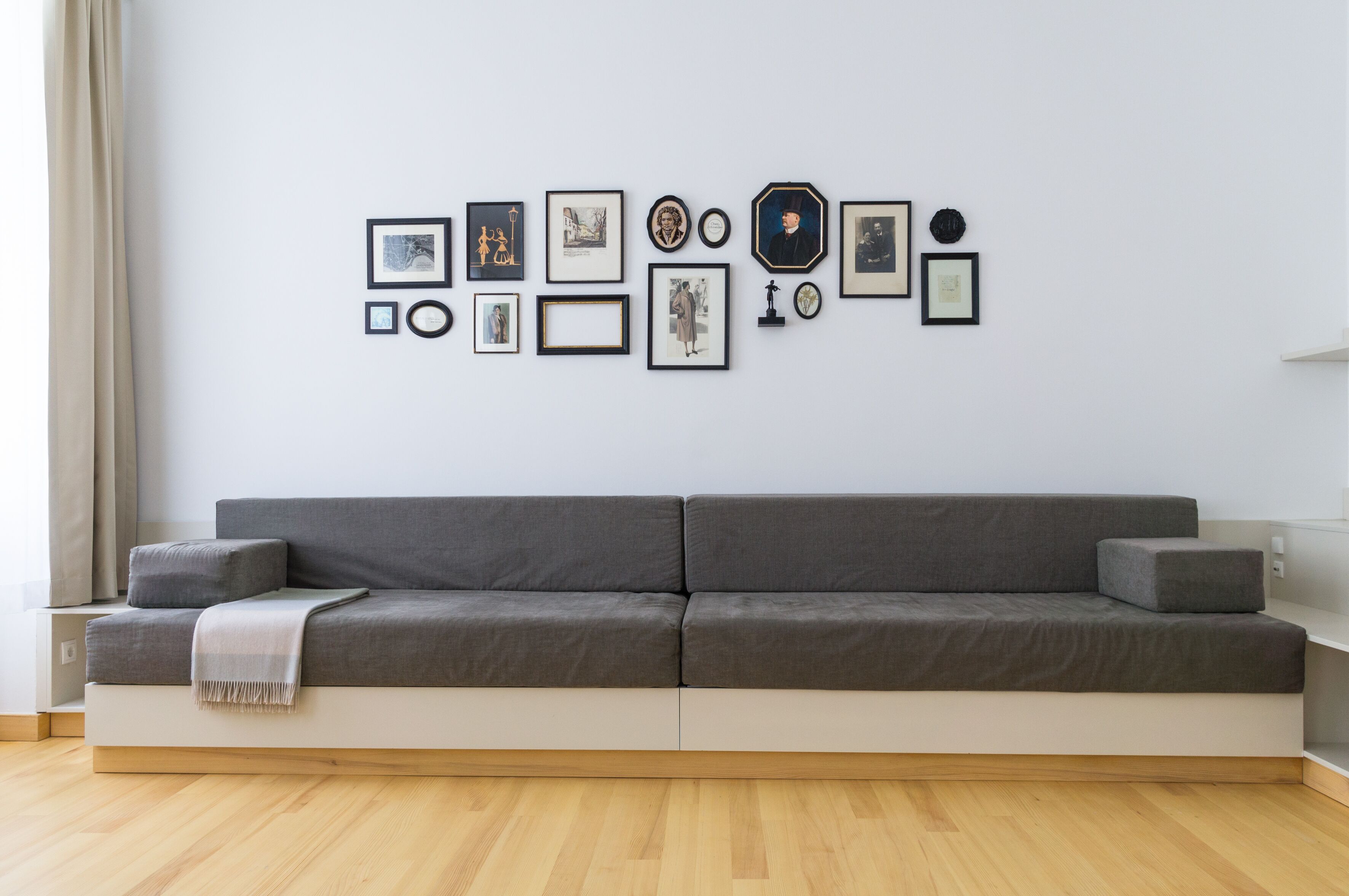 Un salon moderne avec un canapé gris, une table d’appoint blanche et un mur décoré de divers tableaux encadrés.