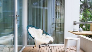 Ein modernes Zimmer mit Glastür, einem weißen, flauschigen Sessel, einem kleinen weißen Tisch und einem Holzboden.