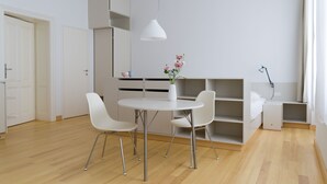 Ein modernes, minimalistisches Zimmer mit einem runden Esstisch, weißen Stühlen, einer weißen Pendelleuchte und integrierten Regalen.