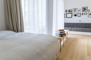 Ein modernes Schlafzimmer mit einem großen Bett, einem Nachttisch mit Büchern, einem grauen Sofa und einer Wand mit gerahmten Bildern.