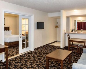 A hotel room with a bed, a small table, a chair, a TV, and a bathroom with a shower and toilet.