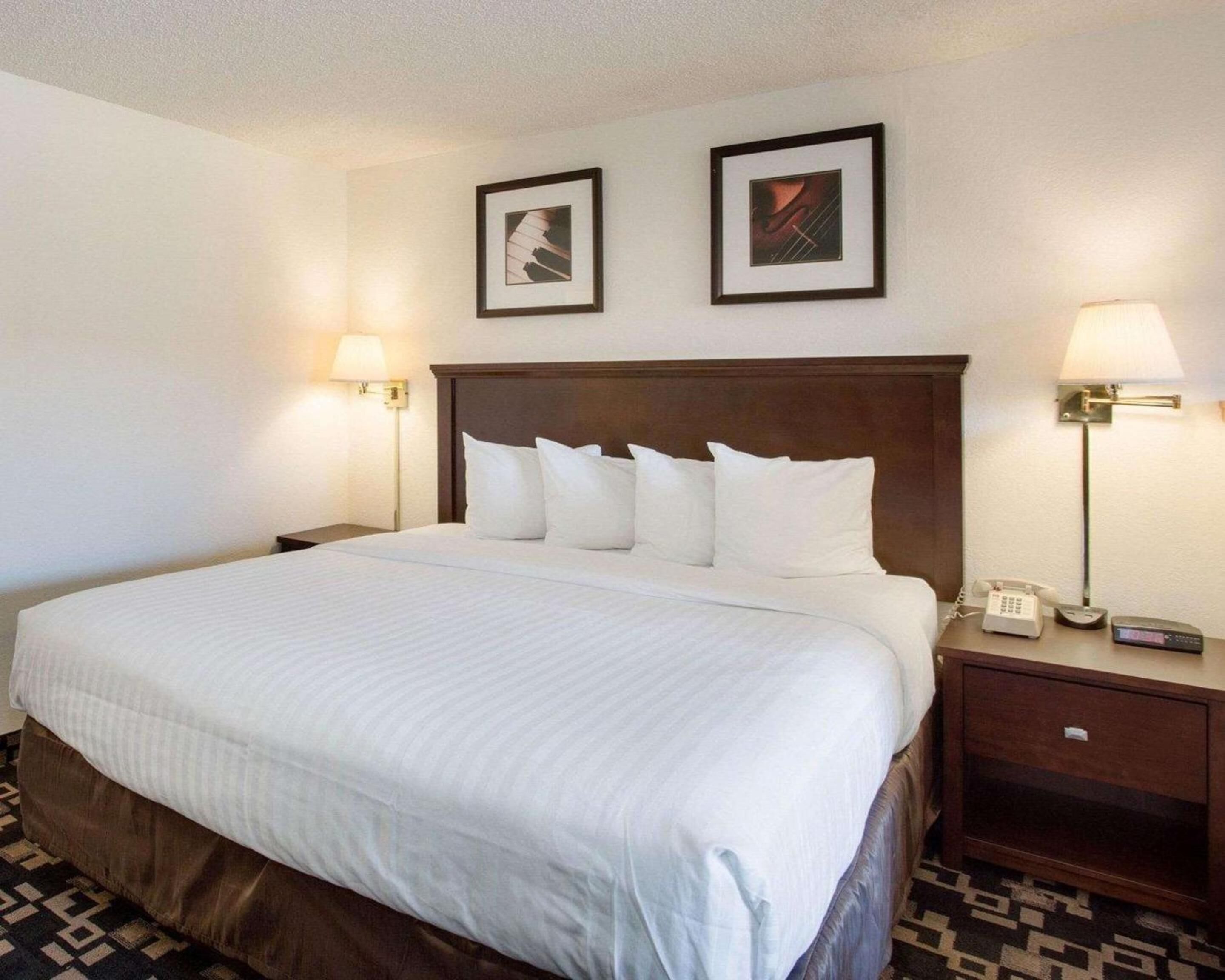 Habitación de hotel con una cama grande, dos mesitas de noche, dos lámparas y dos cuadros en la pared.