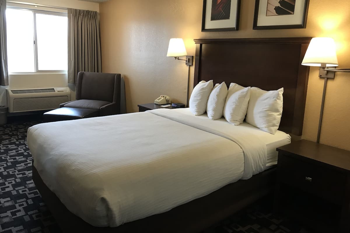 A hotel room with a large bed, two bedside lamps, a chair, a desk with a phone, and a picture on the wall.