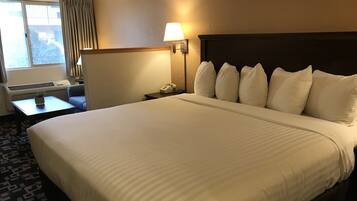 A hotel room with a large bed, a bedside table with a lamp, a telephone, and a window with curtains.