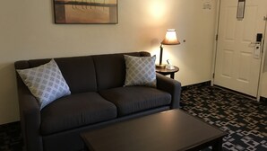 A dark brown sofa with patterned pillows, a small table with a lamp, and a painting of trees on the wall.