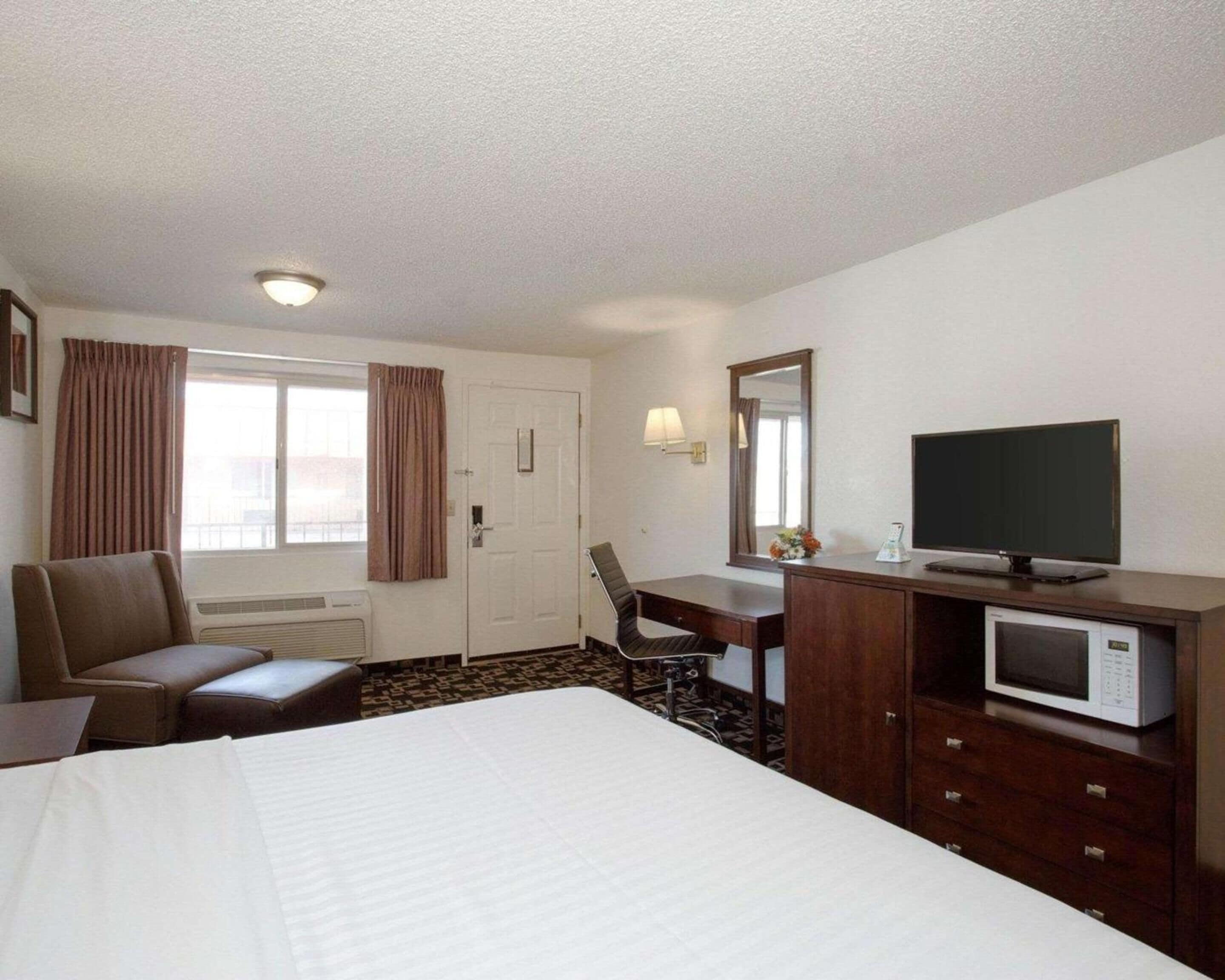 A hotel room with a bed, a desk, a chair, a television, a microwave, and a window with curtains.