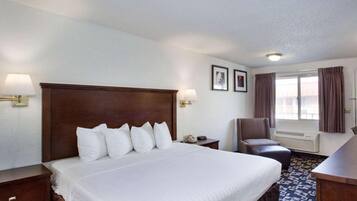 A hotel room with a large bed, a desk, a chair, a lamp, and a window with curtains.