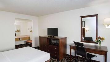 Une chambre d’hôtel comprenant un lit, un bureau avec une chaise, une télévision, une commode, un miroir et une lampe.
