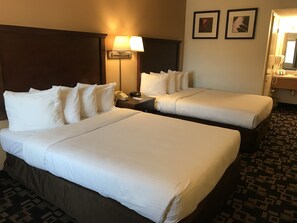 A hotel room with two beds, a nightstand with a lamp, a phone, and a mirror. There are two framed pictures on the wall.
