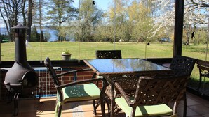An outdoor patio with a glass enclosure, a wood-burning stove, and a view of a grassy area with trees. - Studio with winter garden and lake view - Ferienhof Löschenrand (Bad Saarow)