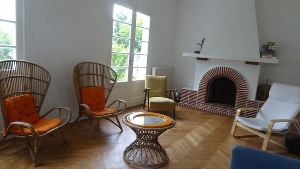 Un salon avec une cheminée, des fauteuils en osier, une table ronde et un canapé bleu.