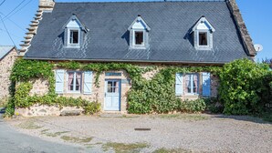 Una casa de piedra con tres ventanas de tejado a dos aguas, una chimenea y hiedra en las paredes.