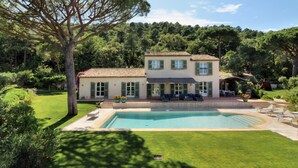Una casa de dos pisos con piscina, rodeada de césped cuidado y árboles.