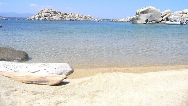 Una playa con agua cristalina, grandes rocas y una orilla de arena.