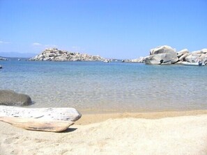 Ein Strand mit klarem Wasser, großen Felsen und einem sandigen Ufer.