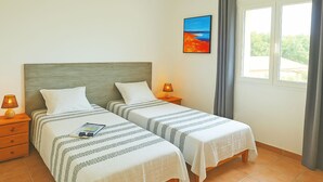 Habitación doble con dos camas, una mesita de noche con lámpara, un cuadro en la pared y una ventana con cortinas.