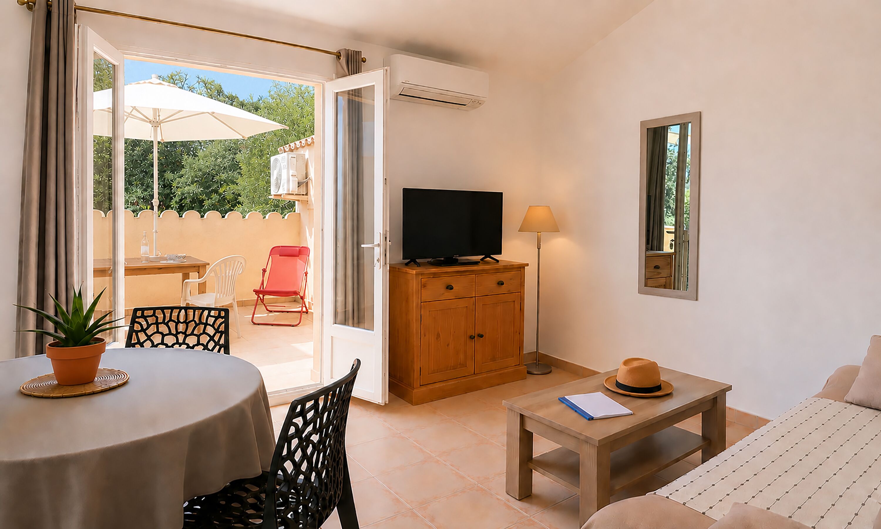 A room with a TV, a table with a potted plant, a chair, a sofa, a small table with a notebook and a hat, and an air conditioning unit.