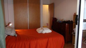 A small, single-bed room with a red bedspread, a wooden wardrobe, and a desk with a chair. - Sunny 2 Bedroom Apartment (Buenos Aires)