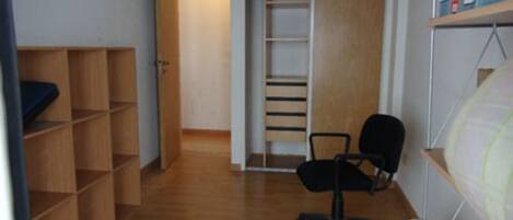 A compact room with a wooden floor, a black office chair, a white shelving unit, and a door leading to another room.