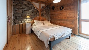 A bedroom with a stone wall, wooden ceiling beams, a bed with a beige bedspread, a nightstand, and a window. - Authentic home, combining the warmth of wood and mountain stone.  (Les Belleville)