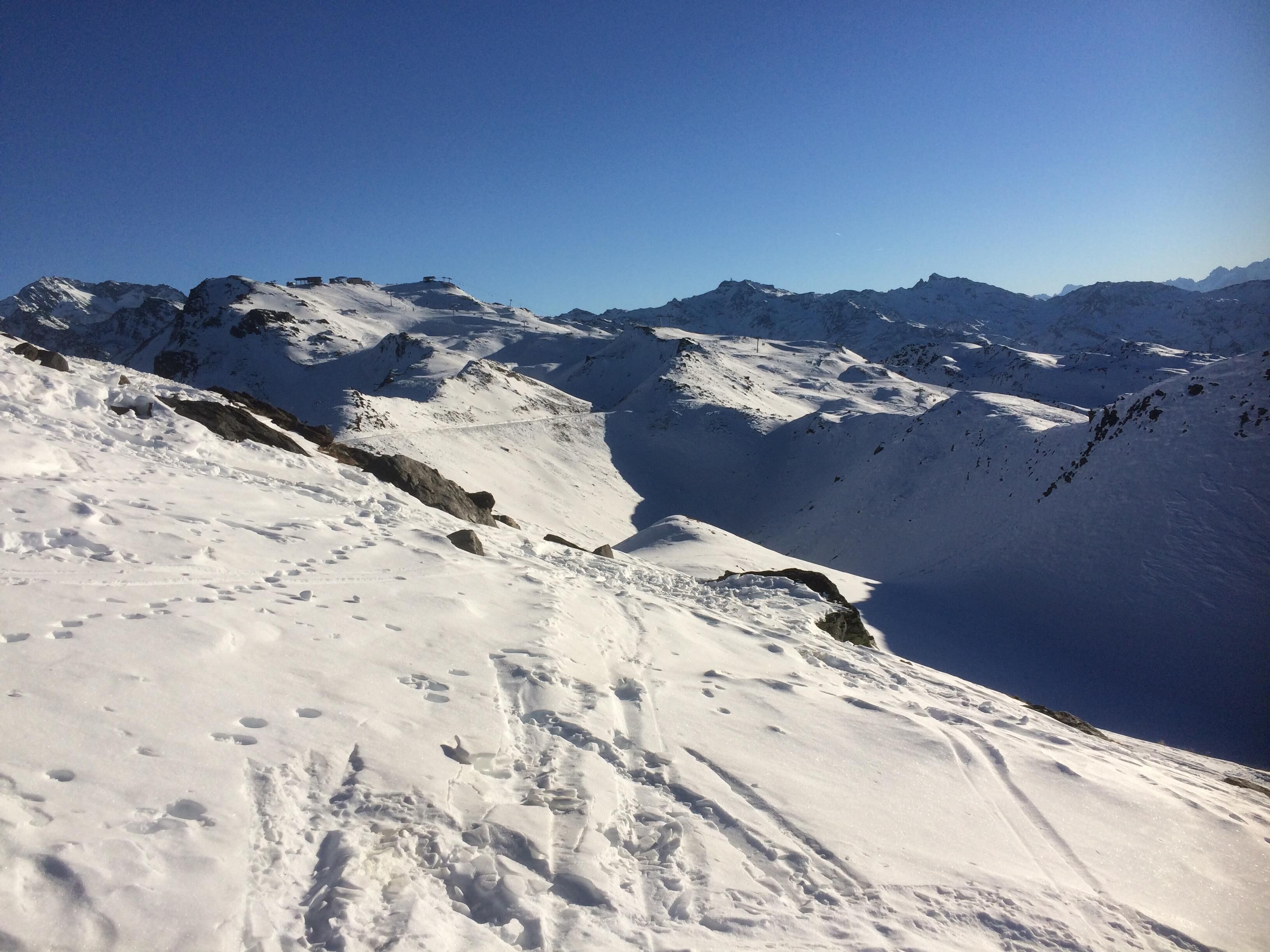 A snow-covered mountain slope with rocky outcrops and a clear blue sky.