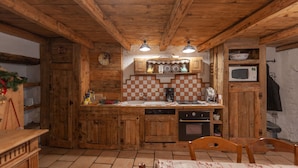 A rustic kitchen with wooden cabinets, a checkered backsplash, and basic appliances. - Authentic home, combining the warmth of wood and mountain stone.  (Les Belleville)