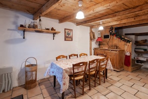 A rustic dining area with a wooden table set for six, surrounded by chairs. A wicker basket is on the floor to the left.