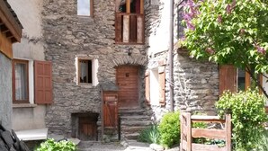 A stone building with multiple windows and wooden shutters, a stone staircase leading to a door, and a garden area with grass and plants. - Authentic home, combining the warmth of wood and mountain stone.  (Les Belleville)