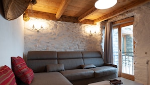 A cozy room with a sectional sofa, a small table, and a stone wall. - Authentic home, combining the warmth of wood and mountain stone.  (Les Belleville)