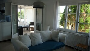 A modern living room with a sofa, a dining area, and a kitchen visible through an open door.