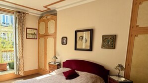 Ein Schlafzimmer mit einem großen Bett, einem Fenster mit Vorhängen, einem Nachttisch und einer Lampe.