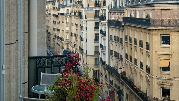 Eine Stadtansicht mit Blick auf den Eiffelturm, mehrstöckigen Gebäuden und einem Balkon mit Außenbestuhlung.