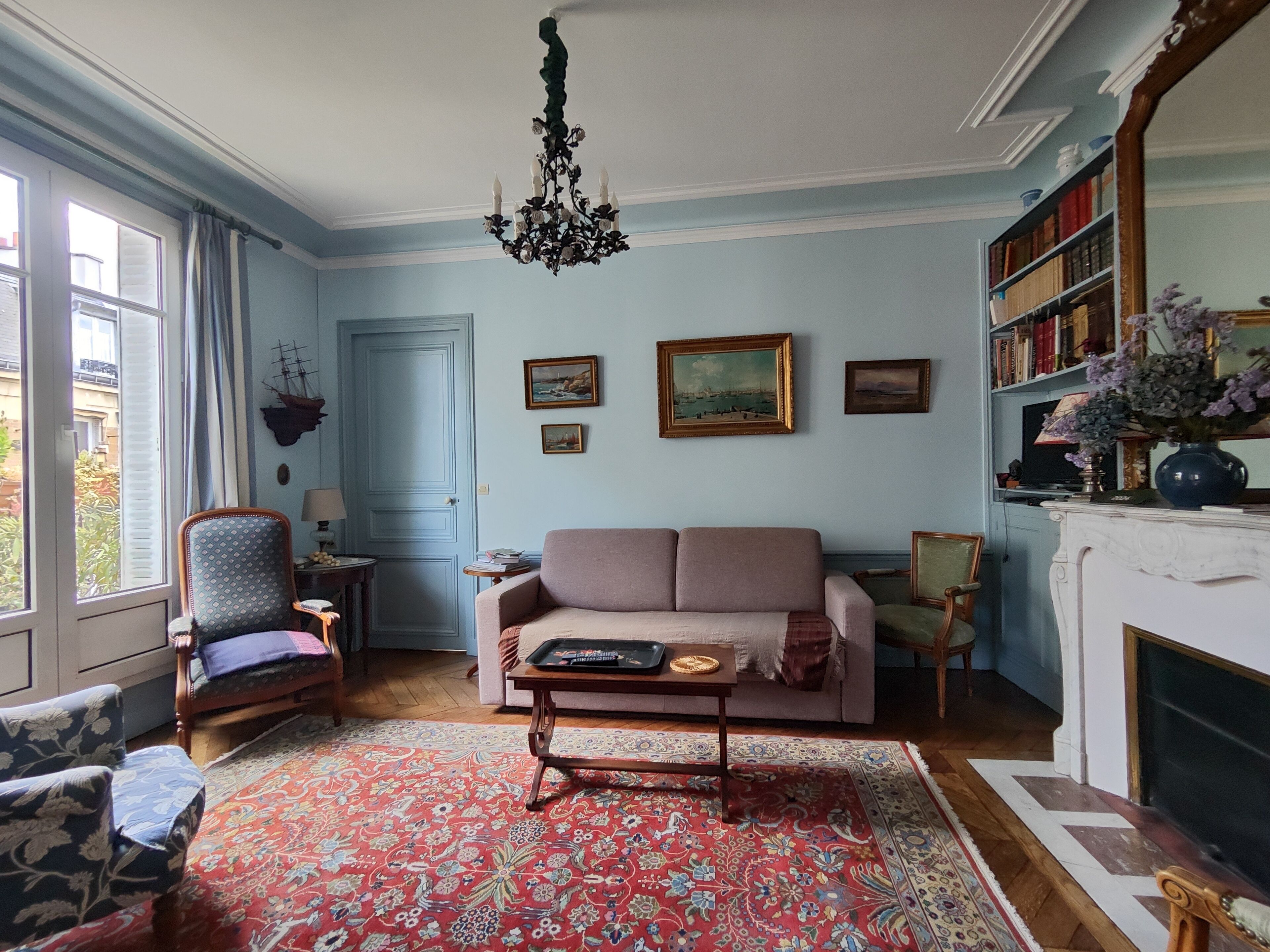 Una sala de estar con sofá, sillones, alfombra estampada, candelabro y chimenea.