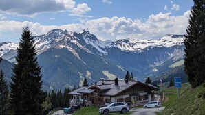 Un chalet de montagne situé au bout d’un chemin de terre, entouré de montagnes enneigées et de pins.