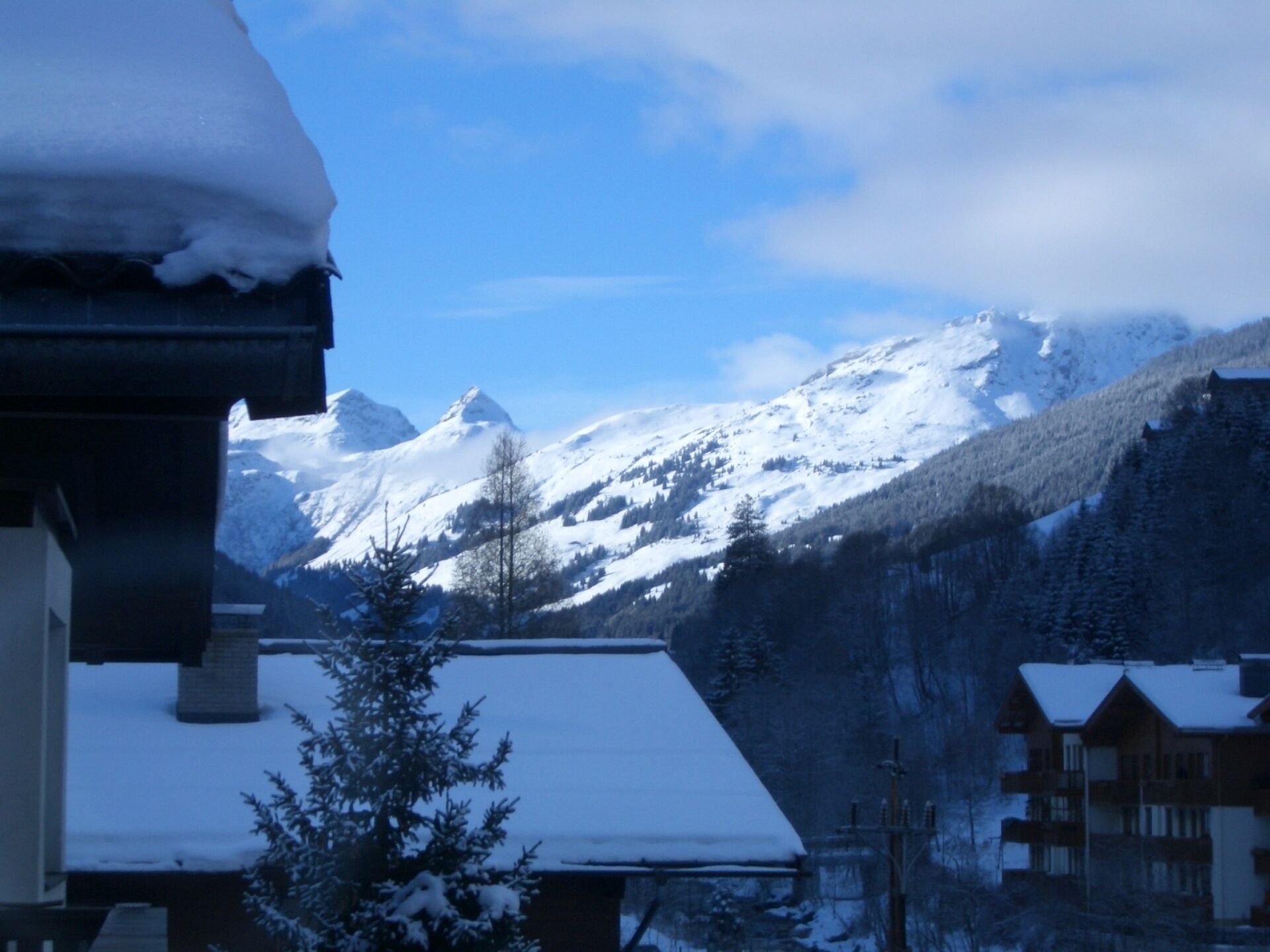 Un paysage montagneux enneigé, avec un bâtiment de style chalet au premier plan.